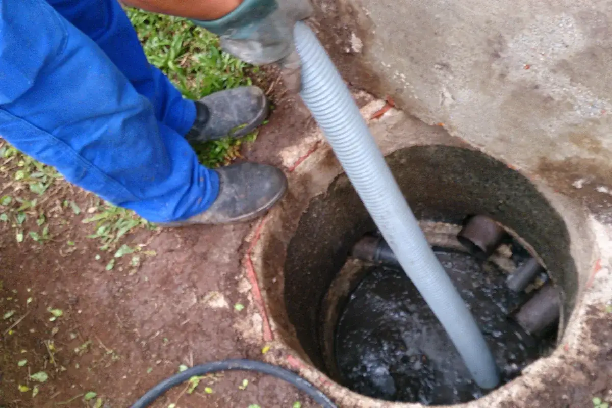 Tanque circular de concreto aberto no quintal, com tubos de entrada e saída visíveis e mangueira de sucção dentro