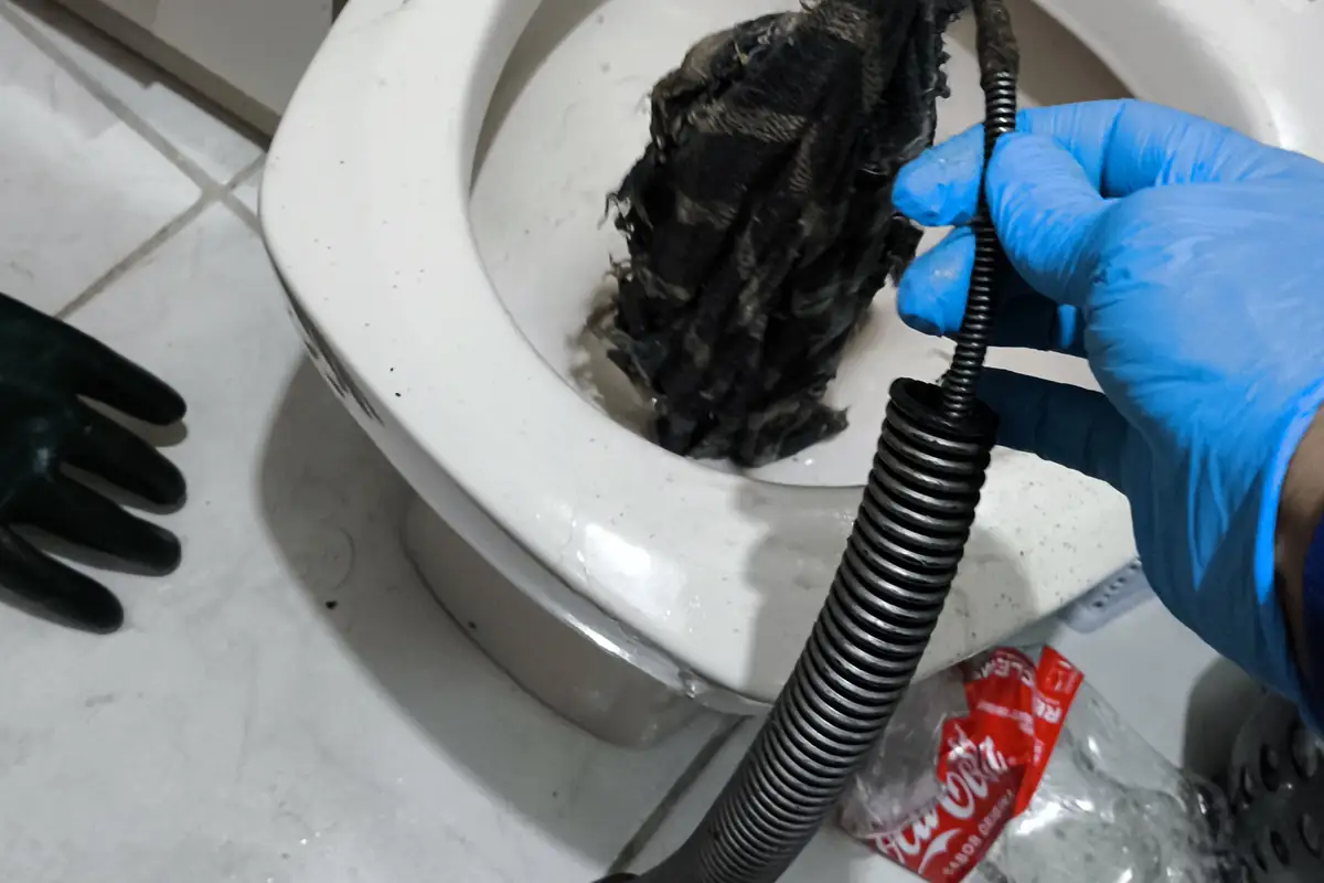 Vaso sanitário com emaranhado de resíduos escuros sendo puxado por mola de desentupimento